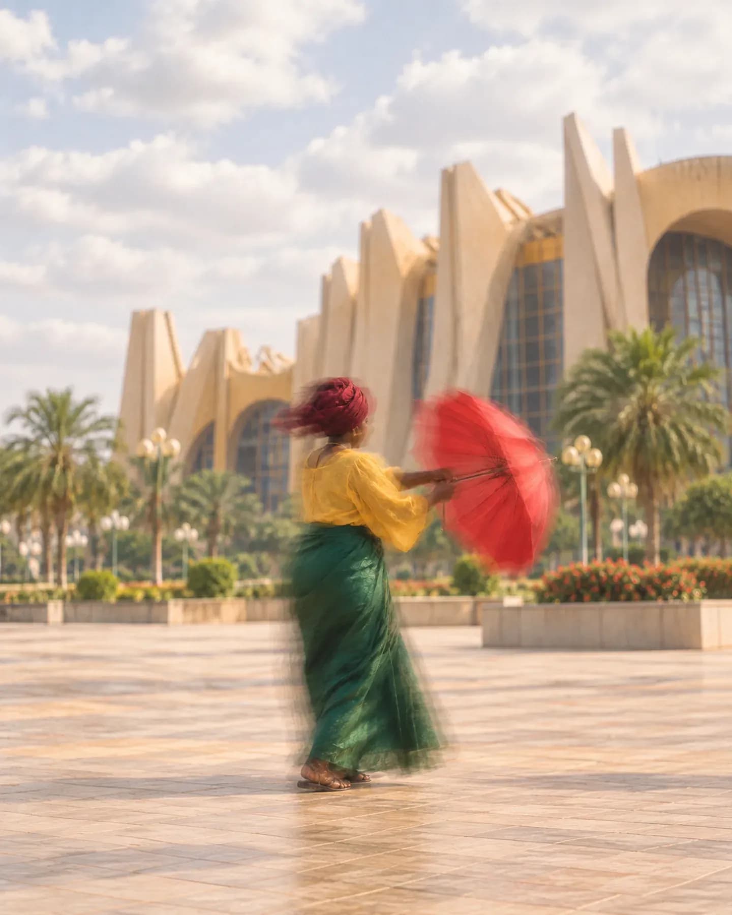 A woman in a yellow blouse and green skirt opens a red parasol outside Salle des Banquets in Ouagadougou.