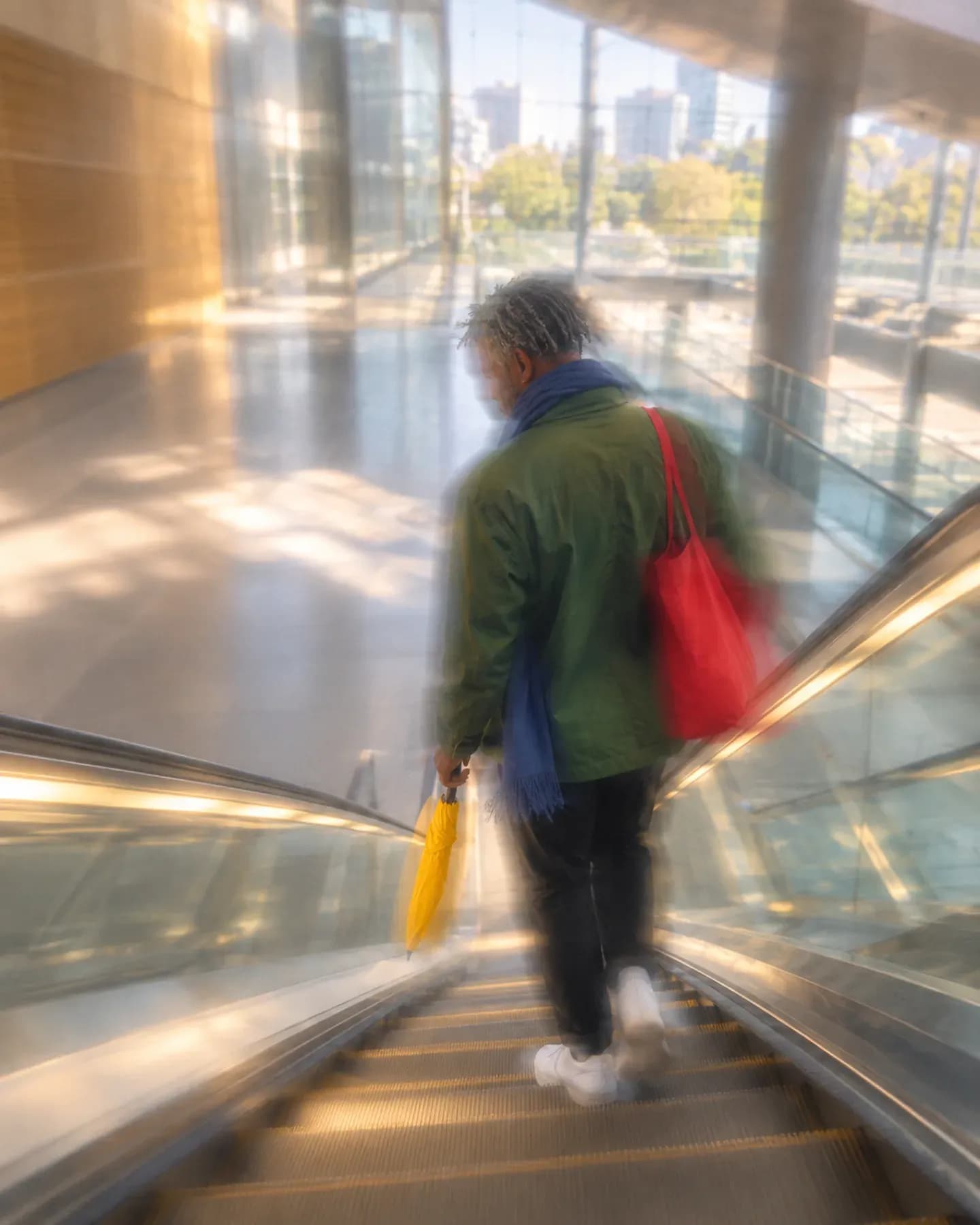 A man in a green jacket carrying a red tote and yellow umbrella descends an escalator at Rosebank Gautrain station in Johannesburg.