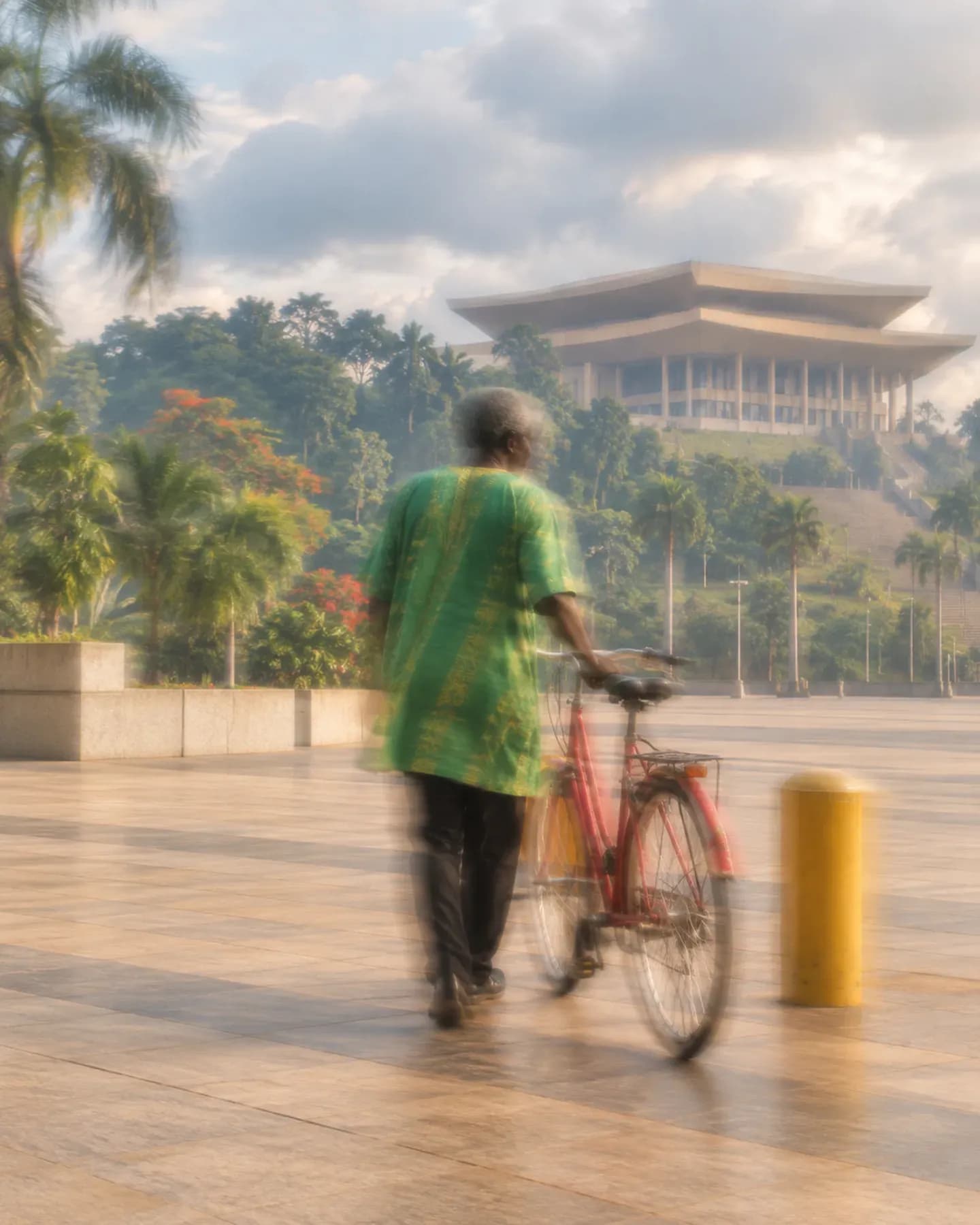 A man in green wheels a red bicycle toward the Palais des Congres in Yaounde.