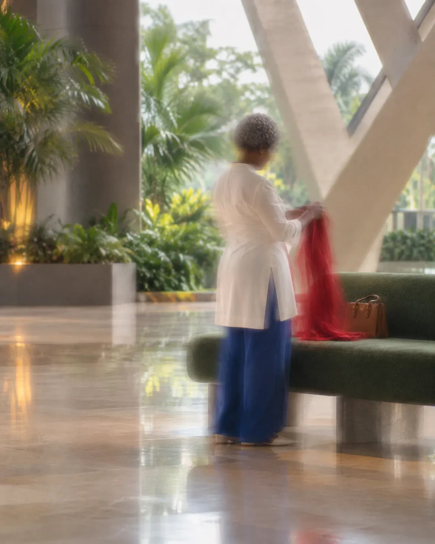 A woman in a white tunic and blue trousers folds a red scarf beside a green bench at Sipopo conference centre in Malabo.