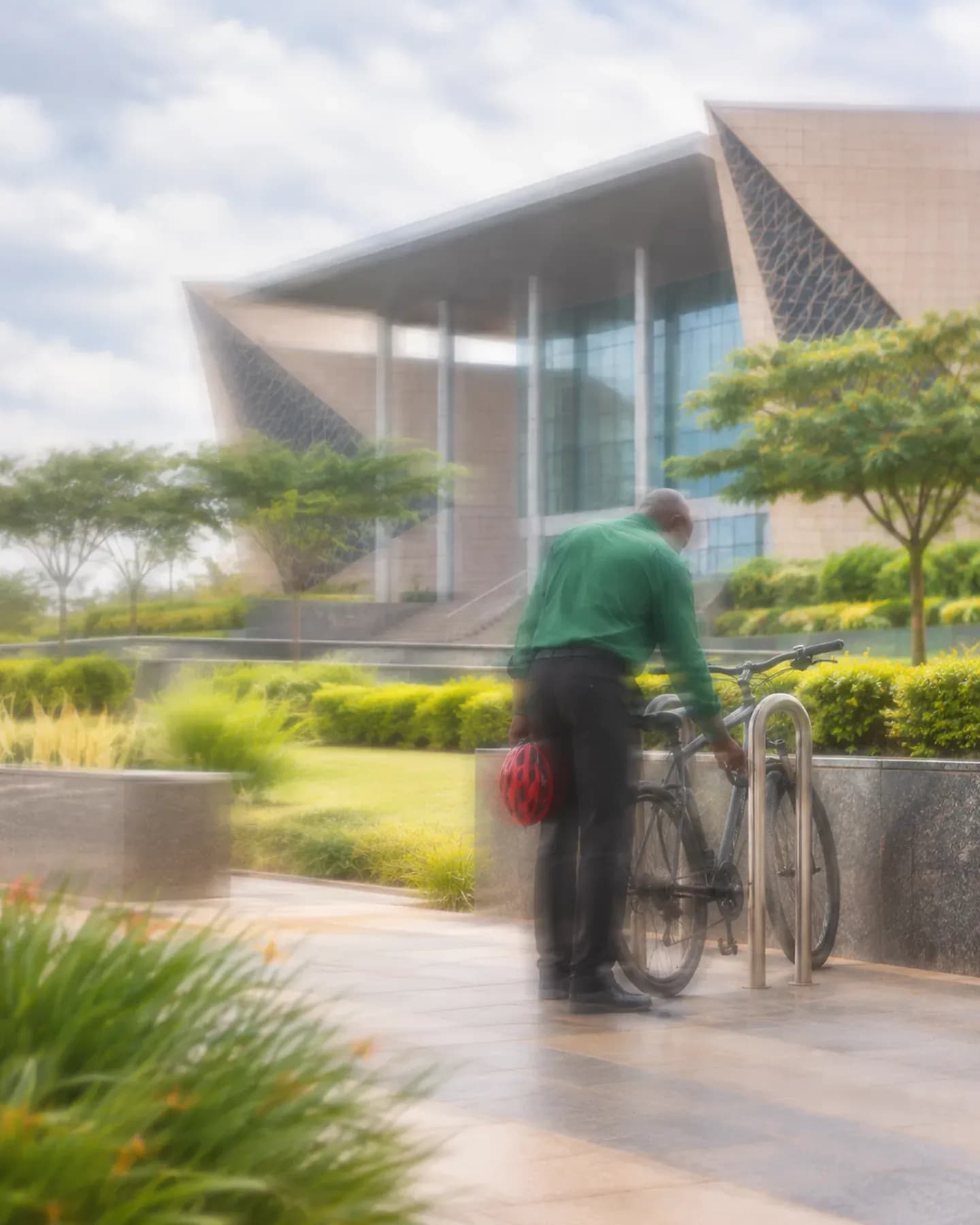 A man in green leans over a bicycle outside Bingu International Convention Centre in Lilongwe.