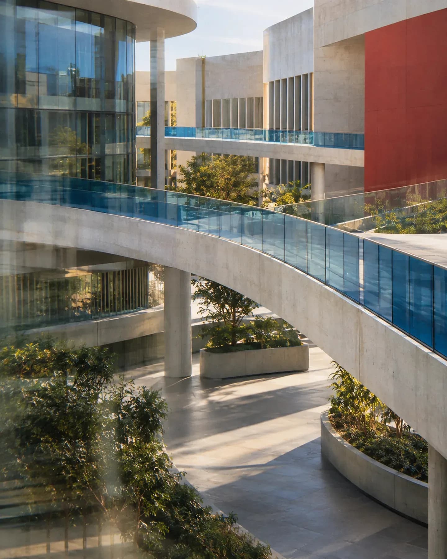 Curved walkways with blue glass railings link modern buildings above a landscaped courtyard.