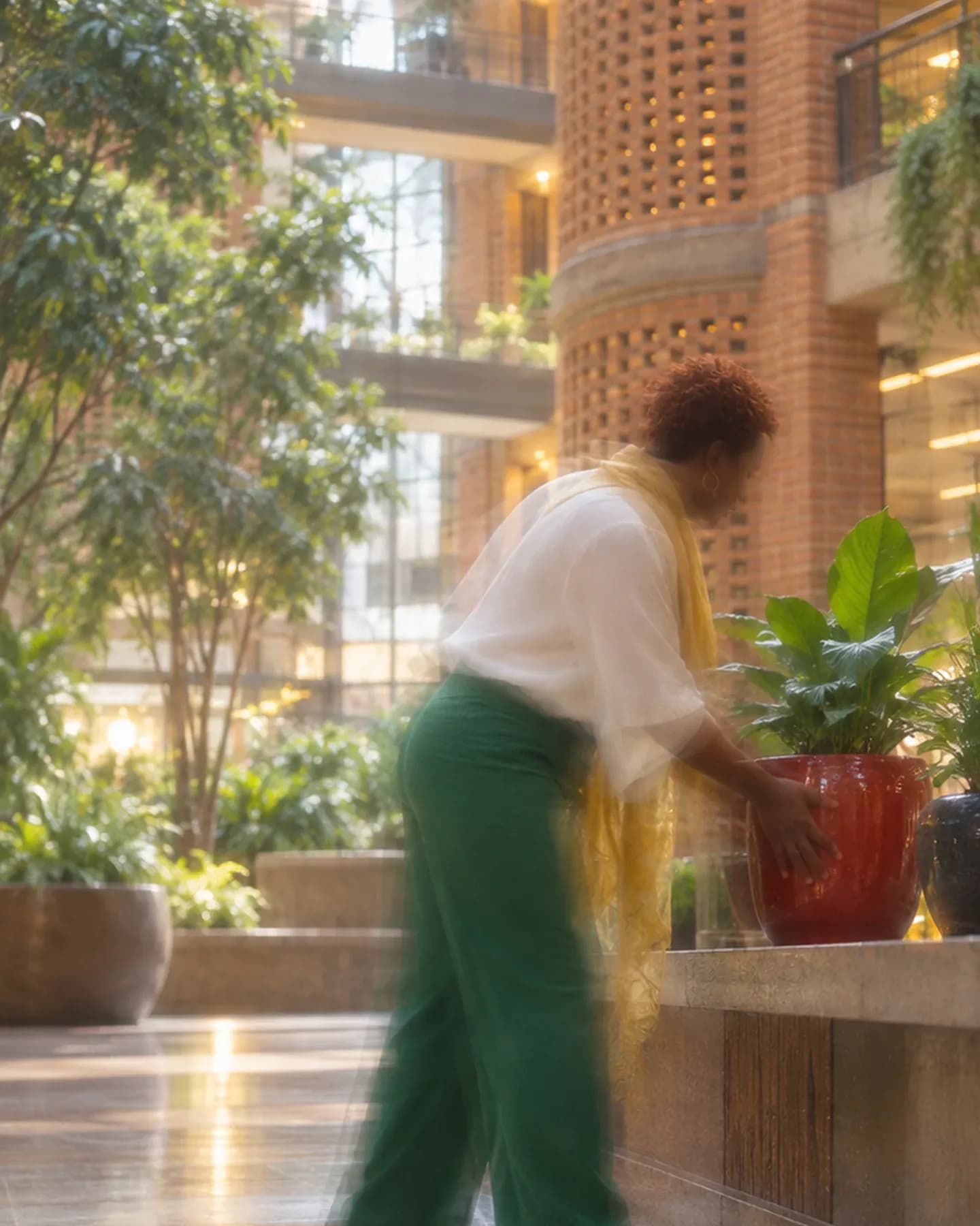 A woman in a white blouse and green trousers places a red planter on a shelf in the brick atrium of Eastgate Centre in Harare.